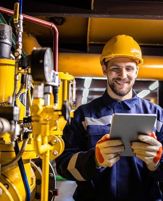 Power plant engineer in safety work wear standing by natural gas installations and pipeline checking consumption on tablet computer application.